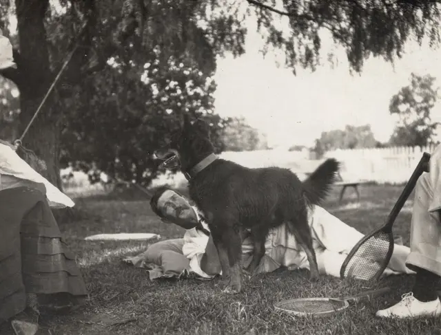 Jack McBratney relaxing with a dog and tennis racquets, circa 1920
